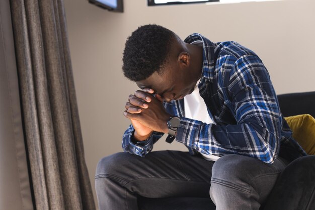 Trauriger afrikanisch-amerikanischer Mann sitzt zu Hause in einem Sessel im Schlafzimmer