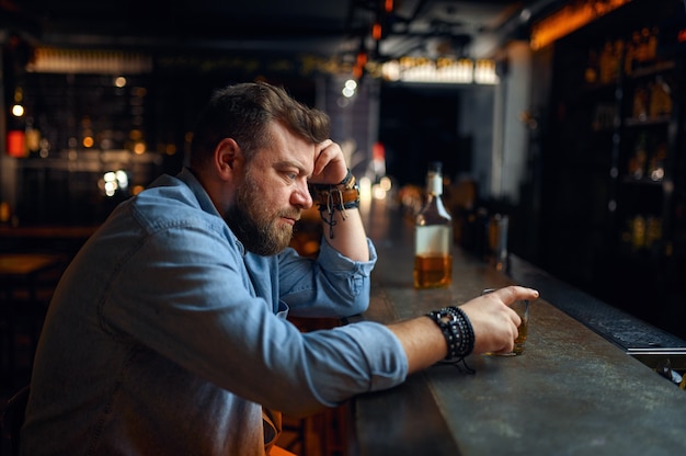 Trauriger bärtiger Mann, der an der Theke in der Bar sitzt. Eine wütende männliche Person in der Kneipe, menschliche Emotionen und Freizeitaktivitäten, Depression, Stressabbau