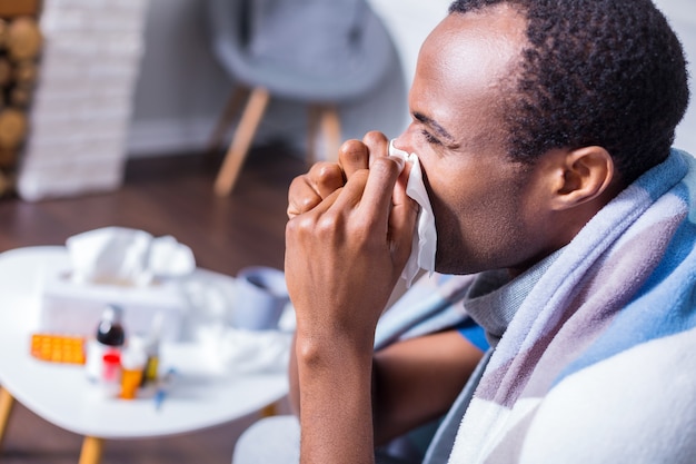 Trauriger depressiver freudloser Mann, der niest und sich unwohl fühlt, während er krank ist