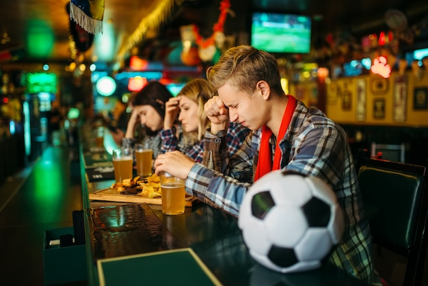 Trauriger Fan bedeckt Gesicht mit Händen in der Sportbar