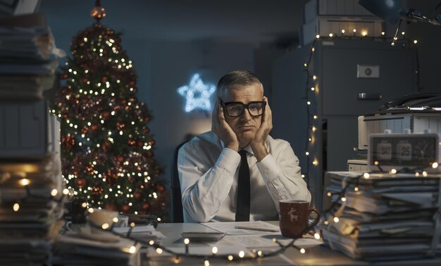 Foto trauriger frustrierter geschäftsmann sitzt am schreibtisch und arbeitet am weihnachtstag