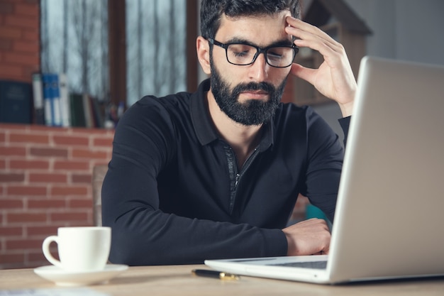 Trauriger Geschäftsmann, der im Computer im Büro arbeitet