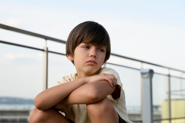 Foto trauriger junge, der im freien sitzt, mittlerer schuss