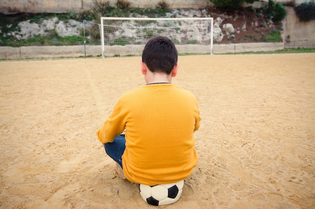 Trauriger Junge, der wartet, um Ball in einem alten Fußballplatz zu spielen