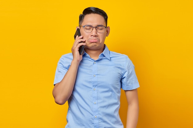 Trauriger junger asiatischer Mann Asiate mit Brille, der am Handy spricht, isoliert auf gelbem Hintergrund Geschäftsmann- und Unternehmerkonzept