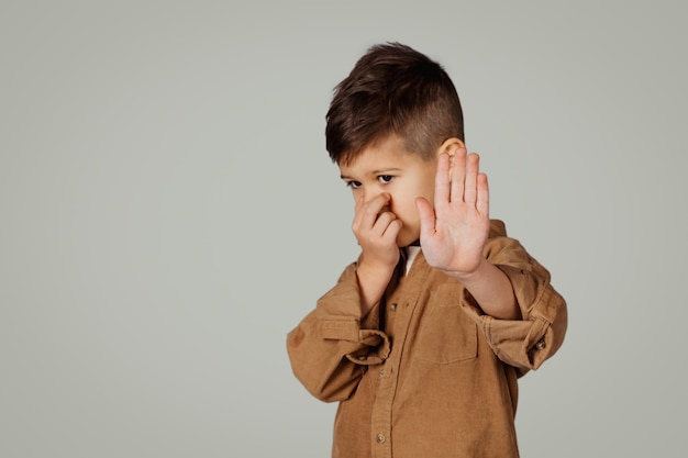 Trauriger kaukasischer Jahre alter kleiner Junge, der die Nase mit der Hand bedeckt, die ein Stoppschild macht