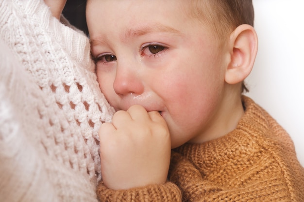 Trauriger kleiner Junge weint. Kleinkind hat Stress, Schmerzen und ist müde. Mutter tröstet ihren weinenden Jungen.