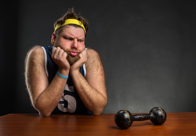 Trauriger Mann, der am Tisch eine Hantel anschaut