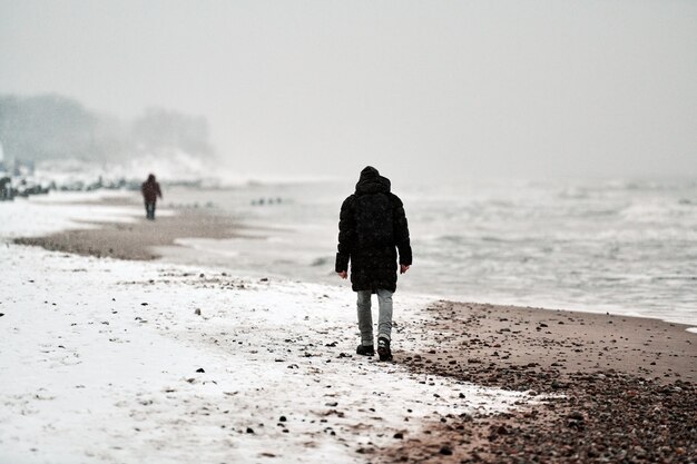 Trauriger Mann in der schwarzen Jacke, die entlang der Seeküste im Winter geht.