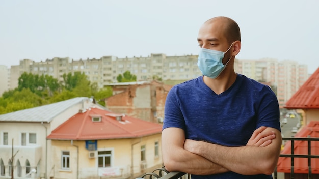 Trauriger Mann mit Einwegmaske auf dem Balkon wegen Coronavirus-Isolation.