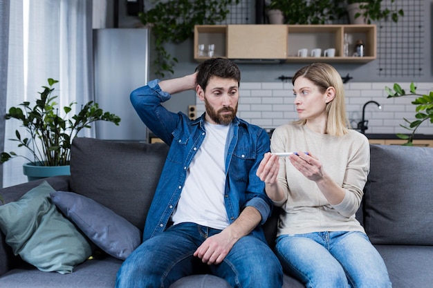 Trauriger Mann und Frau, die auf der Couch sitzen, enttäuscht von einem negativen Schwangerschaftstest