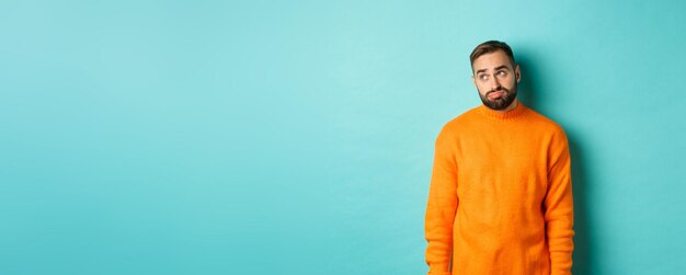 Foto trauriger und düster mann, der sich langweilig sieht, in der oberen linken ecke steht in orangefarbenem pullover gegen die person
