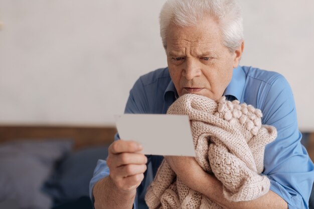 Trauriger unglücklicher älterer Mann, der seine Frau gestrickt hält und eine Notiz liest, während er nostalgische Erinnerungen hat