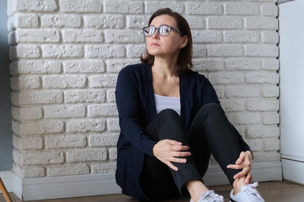 Trauriges depressives Alter einsame Frau, die auf Boden sitzt.