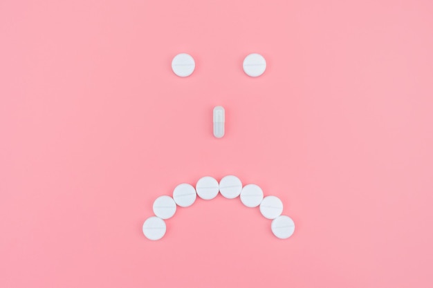 Trauriges Emoticon von medizinischen Pillen auf blauem Hintergrund. Gesundheitsunterstützung. Depressionen mit Antidepressiva behandeln.