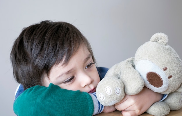 Trauriges Kind, das mit Teddybären mit unglücklichem Gesicht sitzt,