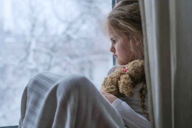 Trauriges Kind hält ein Spielzeug und schaut aus dem Fenster