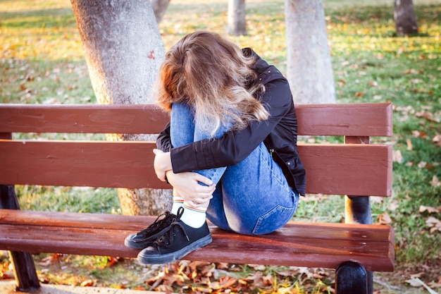 Trauriges Teenagermädchen, das auf der Bank im Herbstpark sitzt. Weinendes junges Mädchen in Depressionen