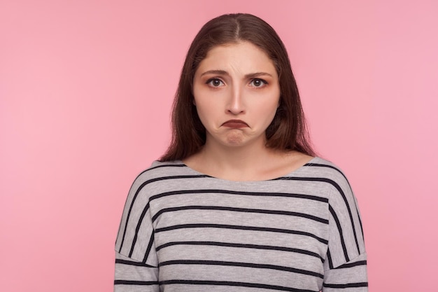 Traurigkeit negative Emotionen Porträt einer unglücklichen depressiven jungen Frau in gestreiftem Sweatshirt, die mit enttäuschtem Ausdruck nachtragend Grimasse aussieht Studioaufnahme isoliert auf rosa Hintergrund