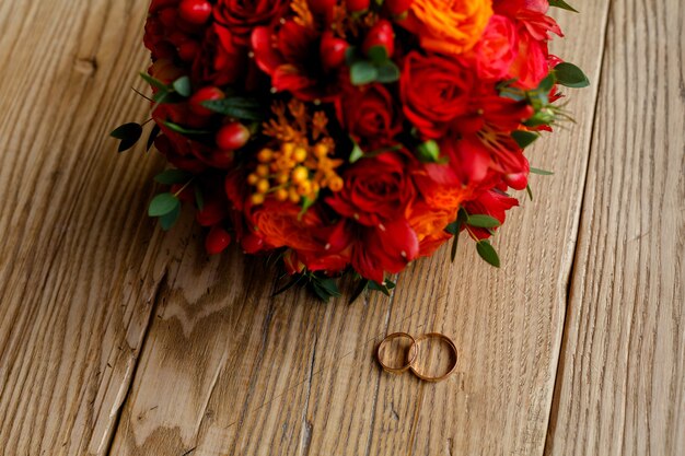 Trauringe und ein Strauß roter Blumen auf Holzuntergrund