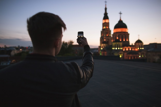 Traveller tira fotos da cidade em um telefone. Turista perto de atrações. Guy usa um gadget digital para fotos