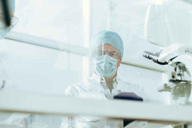 A través del grupo de vidrio de científicos en máscaras protectoras trabajan en el laboratorio.