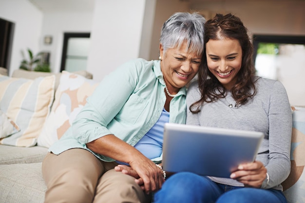 Trazendo a mãe para a velocidade foto de uma jovem mostrando algo para sua mãe em seu tablet enquanto elas se sentam juntas em um sofá