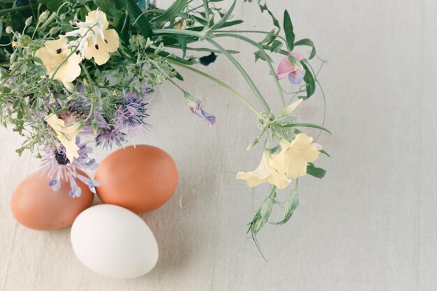 Tre huevos de gallina multicolores sobre un mantel de lino con un ramo de flores silvestres de primavera