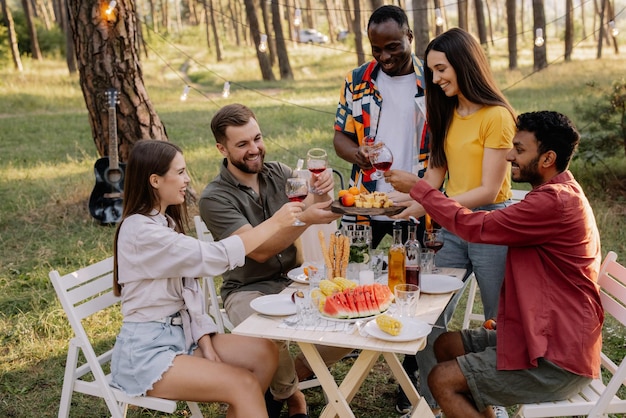 Treffen einer multiracialen Gruppe von Freunden, die während einer Party im Wald essen und Wein trinken