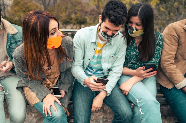 Treffen von Freunden mit Gesichtsmaske, die miteinander reden und ein mit dem Internet verbundenes Smartphone verwenden