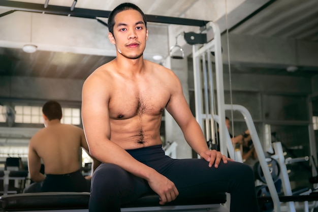 Treiben Sie den muskulösen hübschen asiatischen Mann an, der im Fitnessstudio nach Training stark und gesund lächelt.