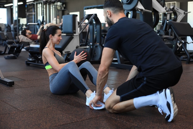 Foto treinador ajudando jovem a fazer exercícios abdominais no ginásio.