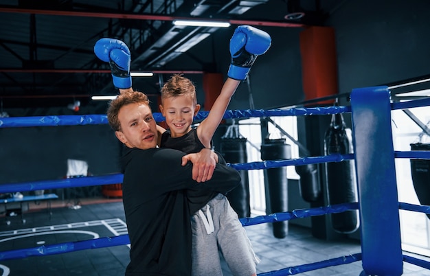 Treinador de boxe em pé no ringue com o menino e comemorando a vitória juntos.