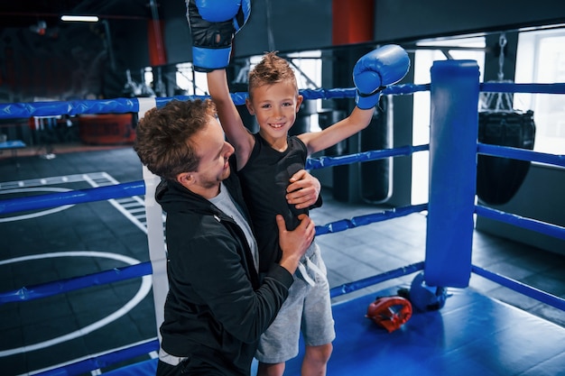 Treinador de boxe em pé no ringue com o menino e comemorando a vitória juntos.