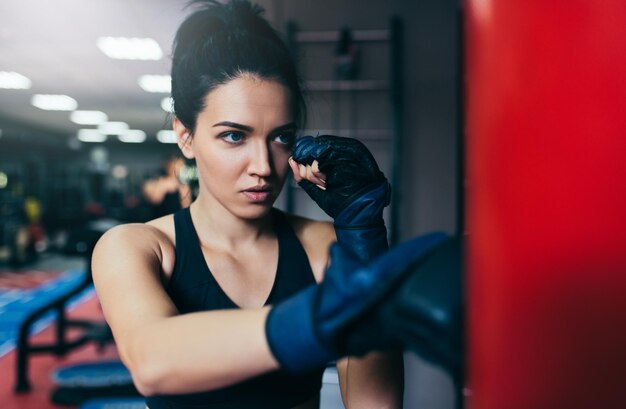 Treinador de esportista morena linda caucasiana socando um saco vermelho com luvas de kickboxing na academia estilo de vida e motivação esportivos