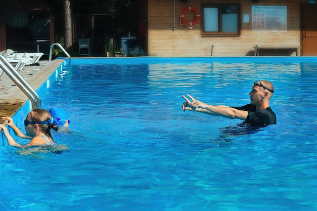 Treinador de natação dando aula com duas garotas na piscina ao ar livre de água azul em dia quente e ensolarado