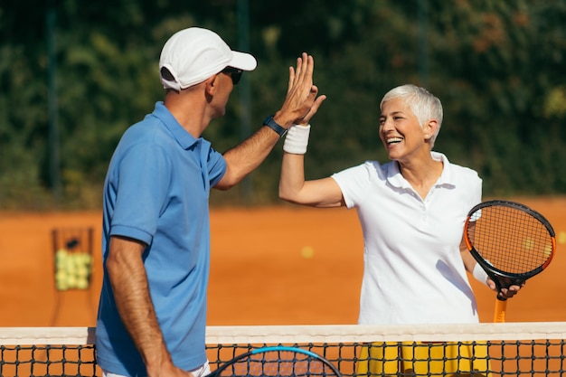 Treinador de tênis praticando serviço com mulher idosa na aula de tênis ao ar livre dando mais cinco