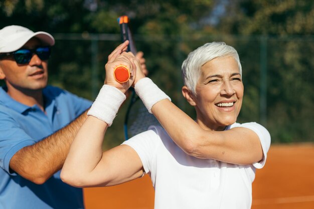 Foto treinador de tênis praticando serviço com uma mulher idosa em aula de tênis ao ar livre