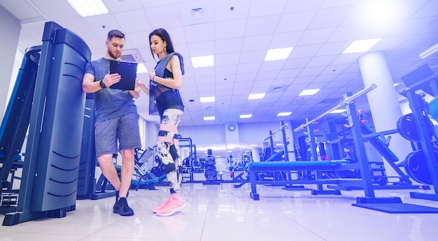 Treinador e sua cliente feminina atraente discutindo programa de treino na academia Instrutor de fitness pessoal Treinamento pessoal