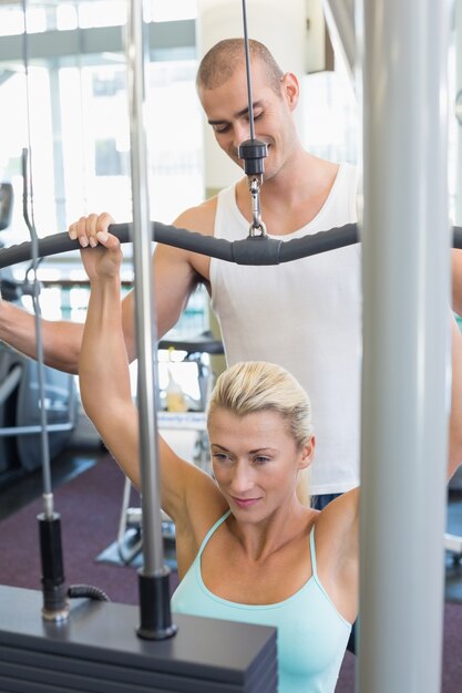 Treinador masculino assistindo mulher na máquina lat na academia