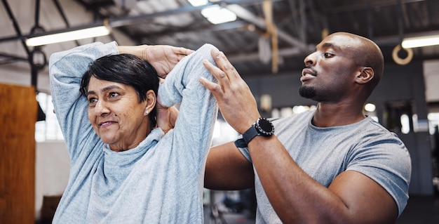 Treinador personal trainer e mulher sênior esticando braços na academia com homem negro para flexibilidade Treinamento em fisioterapia e mulher idosa com treinador ajudando com exercícios e exercícios para a saúde