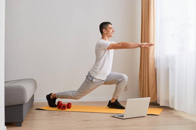 Treinador pessoal Foto de corpo inteiro de instrutor de fitness masculino esticando seu corpo enquanto transmite uma aula de vídeo sobre treinamento em casa usando laptop