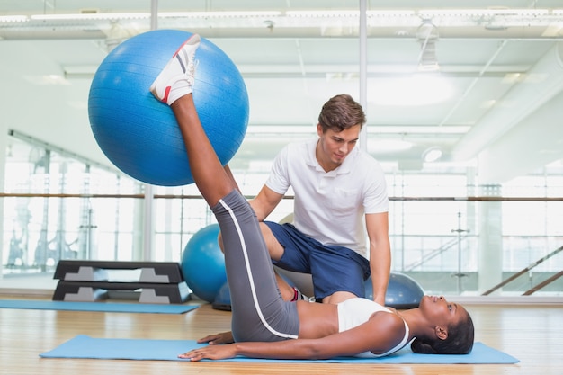 Treinador pessoal trabalhando com o cliente segurando bola de exercícios