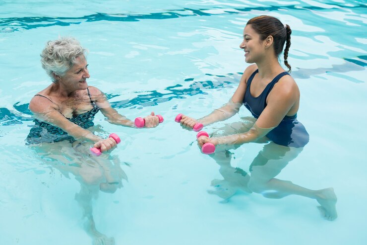 Foto treinadora ajudando mulher idosa a levantar halteres na piscina