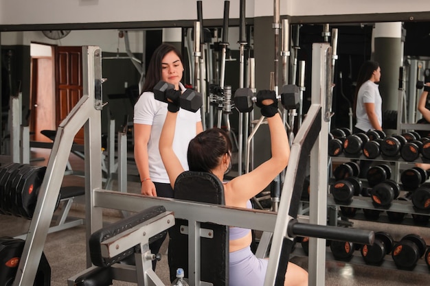 Treinadora observando a técnica de seus alunos enquanto realiza exercícios de ombro com halteres