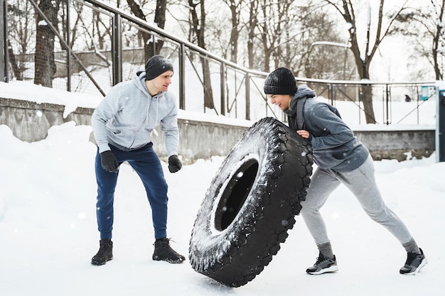 Treinamento cruzado fora Treinador de homem e cliente de mulher durante o treino com um pneu durante o inverno frio e o dia de neve