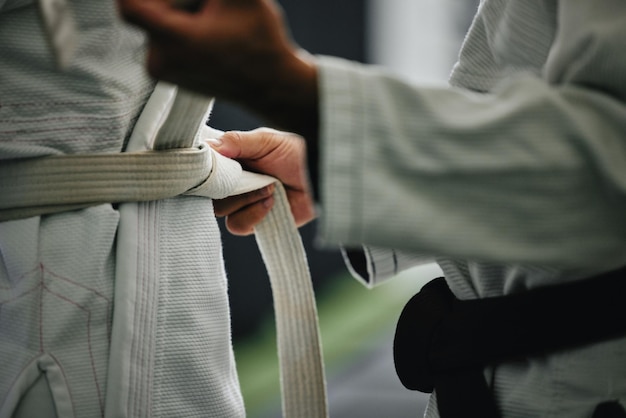 Treinamento de aprendizado de karatê e treino de um estudante de esporte e treinador se preparando para uma aula de luta Mãos de especialistas em defesa amarram um cinto em um estúdio de treino dojo ou clube de bem-estar prestes a trabalhar em fitness