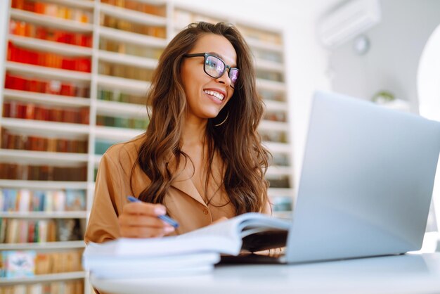 Treinamento de conferência on-line Aluna trabalhando com laptop aprendendo na biblioteca da faculdade Freelance