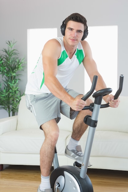 Treinamento de homem bonito e contente em bicicleta de exercício, ouvindo música