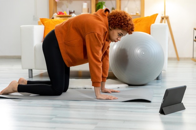 Treinamento de treino de fitness Jovem garota africana saudável fazendo exercícios esportivos no tapete de ioga no chão em casa Mulher atlética em roupas esportivas tem treino para perda de peso Esporte e fitness